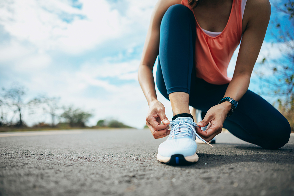 Woman leaned over tying her white running shoes.