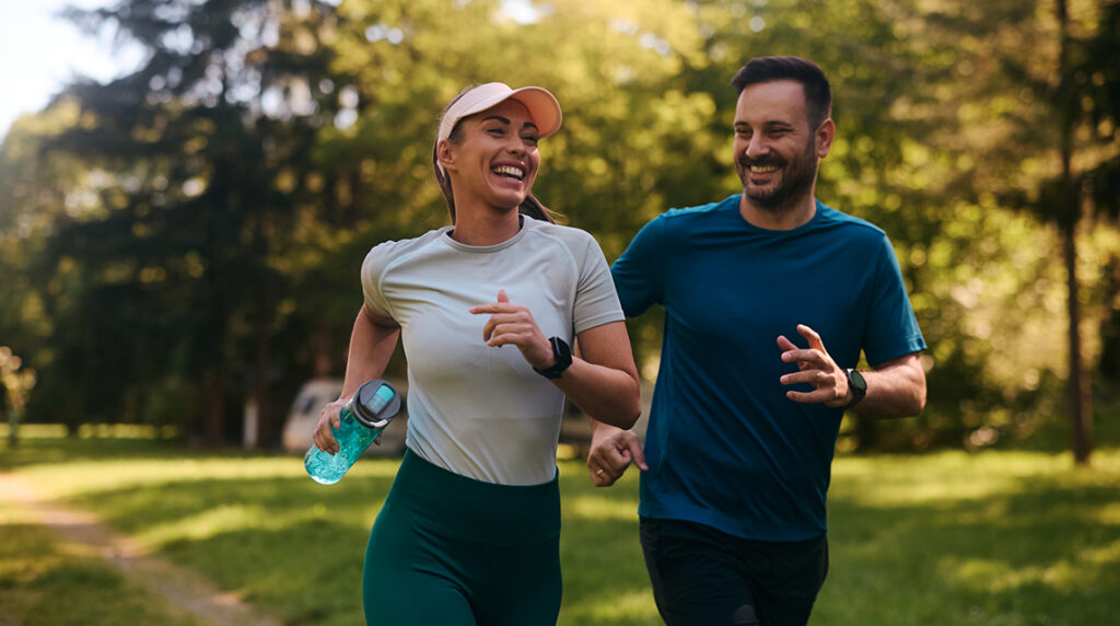Cheerful athletic couple jogging together through a park on a sunny day, symbolizing motivation and the joy of running.