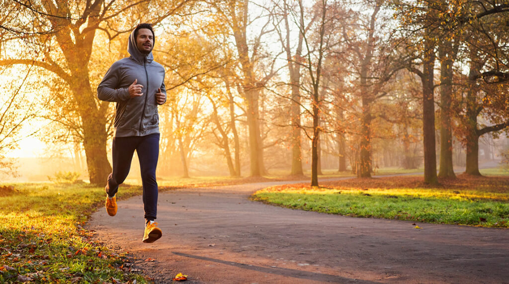 Man running on a road with fall leaves on the pavement.