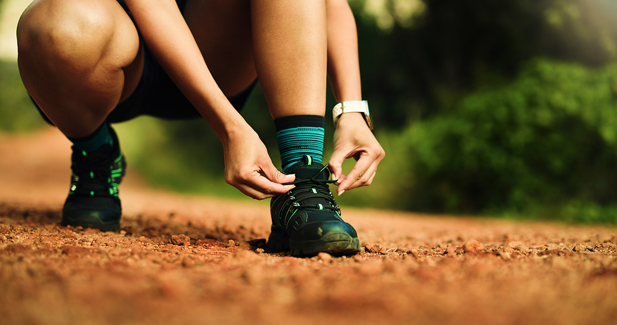 A person tying their running shoes on gravel trail.