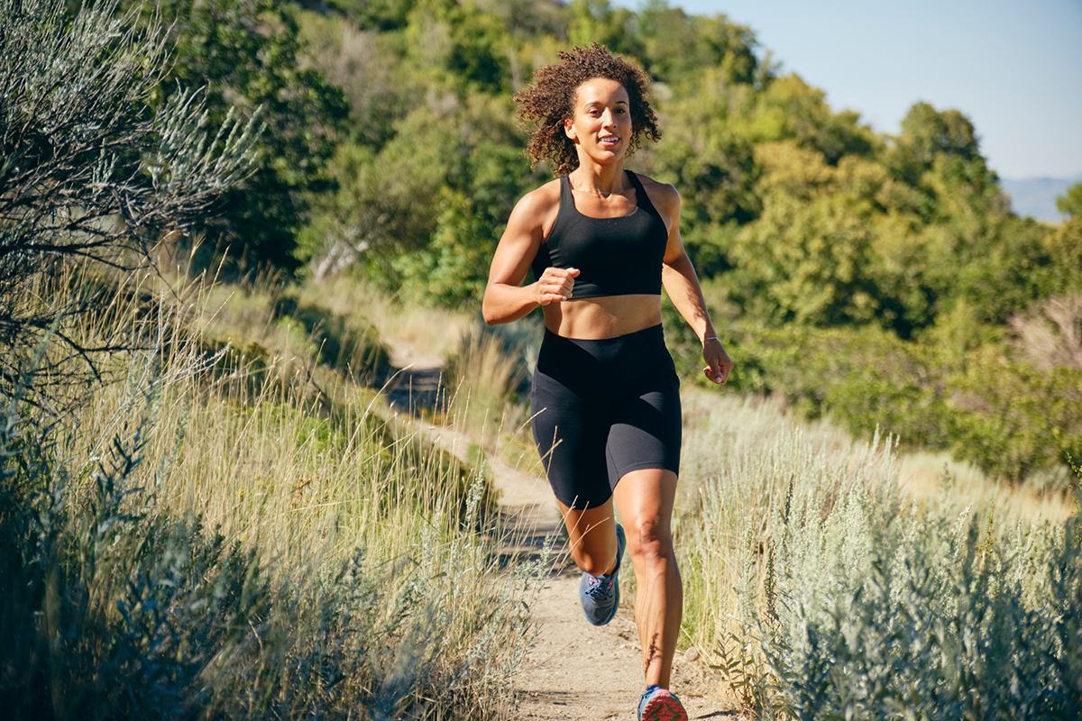 A woman running along a trail on a grassy hillside.