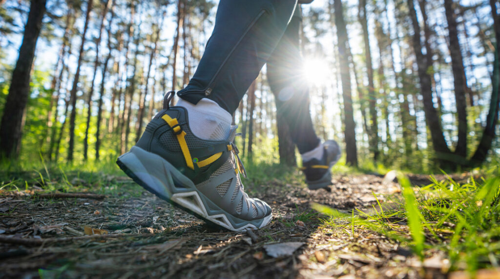 A close-up of a pair of trail running shoes on a person jogging through the woods.