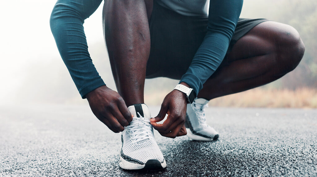 A man crouches down and ties one of his carbon plated running shoes while jogging on a track.