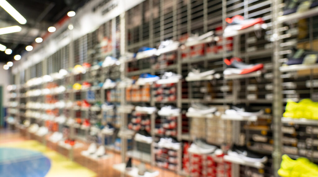 Abstract blurred sustainable sneaker display on store shelves showing rows of athletic shoes in a retail shop environment.
