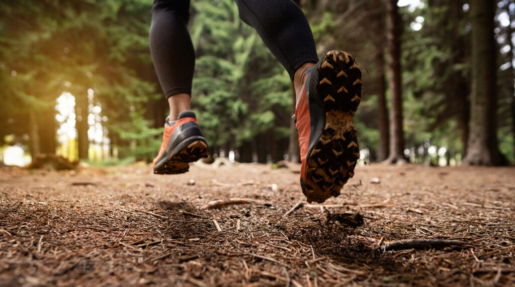 Person running through forest trail wearing cross country running shoes on rugged terrain.