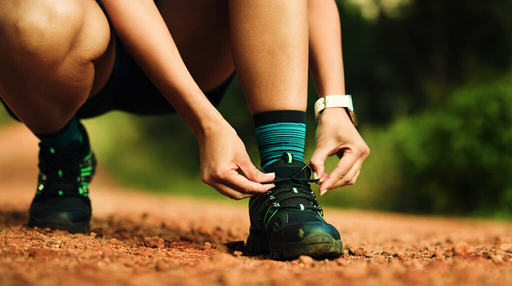A person crouched down and tying their running shoes on a trail.