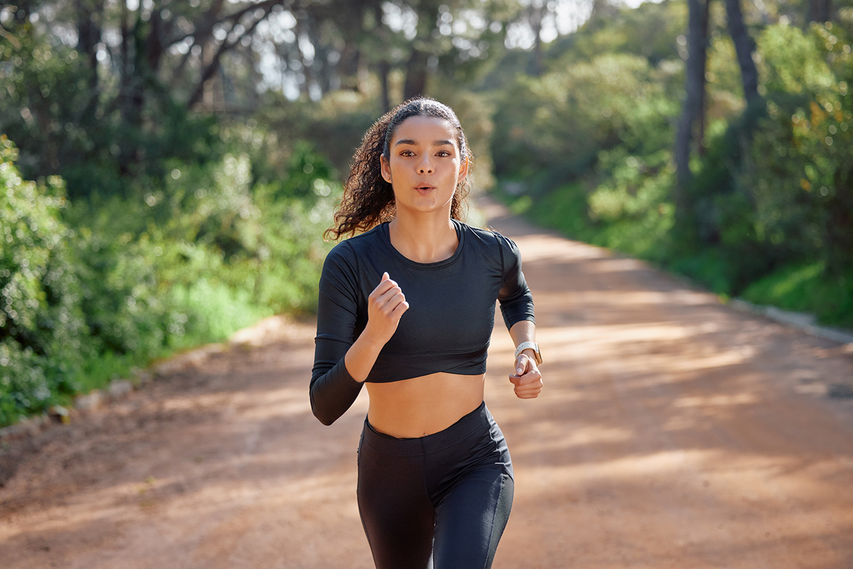 A young woman wearing black activewear jogs on a trail in the woods.