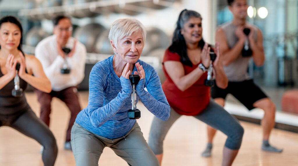 An older woman is lifting weights in a group fitness class at a fitness studio.