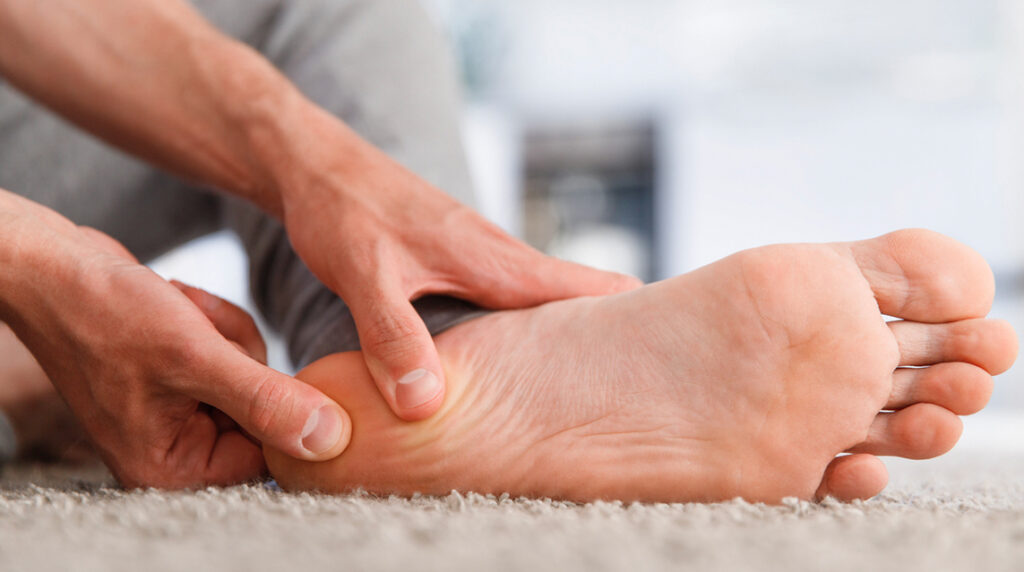 Man sitting on floor massaging heel to relieve plantar fasciitis pain before a run.