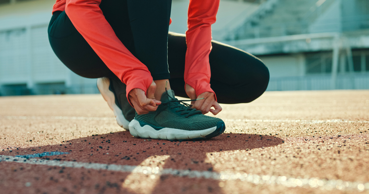 Female runner tying running shoe laces outdoors preparing for a jog.