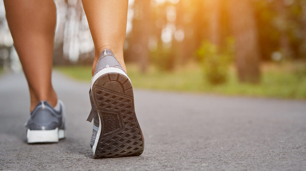 A person walking in walking shoes on a concrete path.