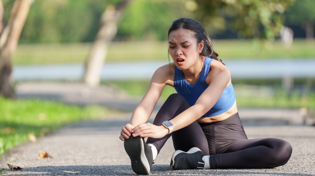 An athletic woman sitting on the ground, holding her foot in pain from a running injury.