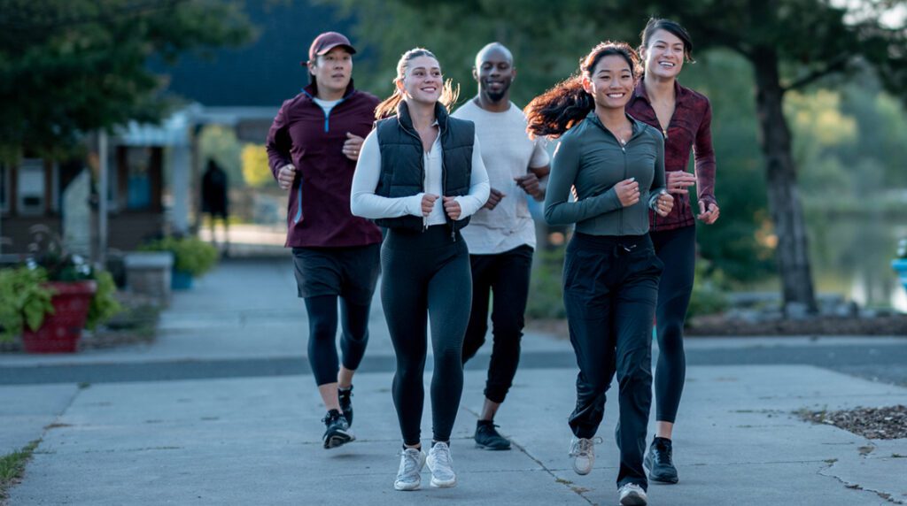 Men and women of diverse backgrounds running together on a tree-lined park trail, embracing fitness, unity, and the joy of outdoor running.