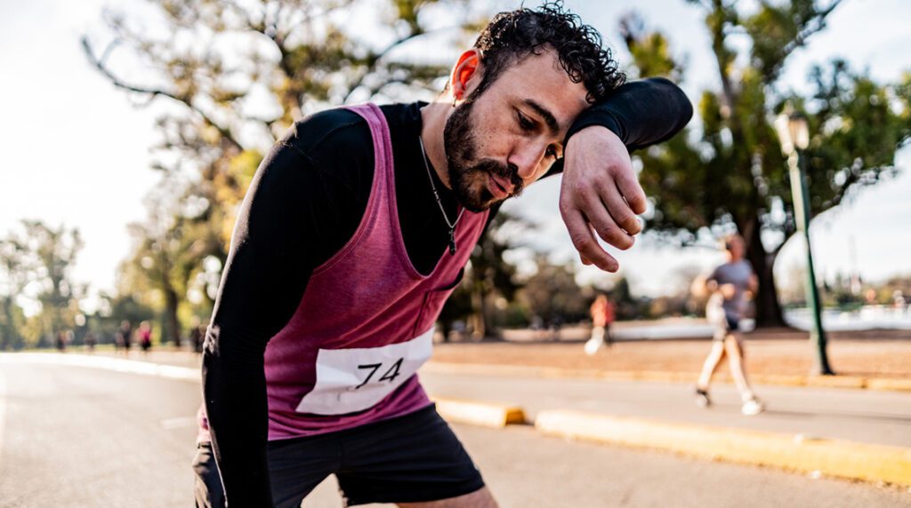 A man wipes sweat from his brow while running in the heat